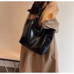 Detail of black faux leather tote bag with gold metal buckle and sleek texture on shoulder