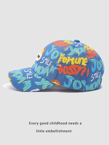 Détail d'une casquette enfant bleue avec motifs graffiti et un patch rond en caoutchouc