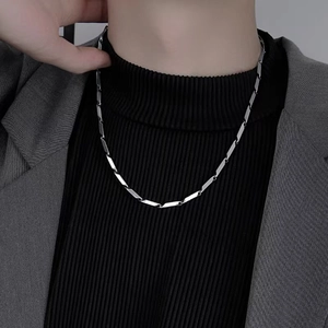 Détail d'une chaîne géométrique en argent portée sur un col roulé noir pour un look chic