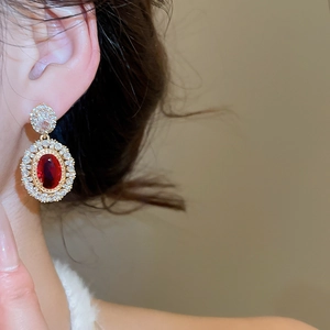 Detailed close-up of vintage gold earrings with oval red ruby and white zircon halo