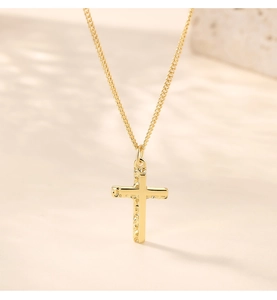 Macro detail of gold cross pendant with hammered texture edges and fine link chain