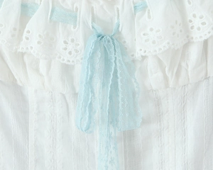 Detailed macro view of white cotton fabric with light blue lace bow and floral embroidery