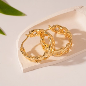 Close-up of gold chain earrings with zircons on a decorative plaster tray background