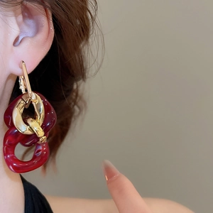 Close-up of interlocking red resin and gold geometric hoop earrings on a model