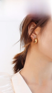 Close-up of golden crossover intertwined stud earrings worn by a model in soft light