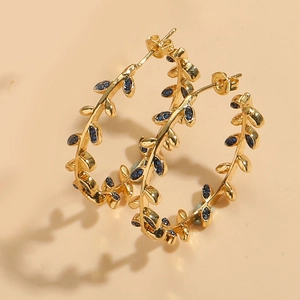 Macro detail of 14K gold-plated leaf earrings with vine patterns and blue crystal accents