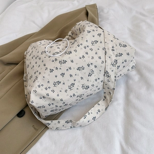 Floral drawstring tote bag with blue patterns on cream fabric placed on a khaki blazer