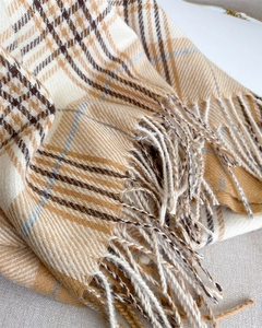 Detailed macro view of the soft plaid cashmere-like fabric texture and fine fringe tassels