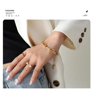 Detailed shot of chunky gold link bracelet with Lucky charm and pearl rings on a model