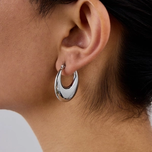 Polished silver stainless steel hoop earrings worn by a model in a close-up professional shot