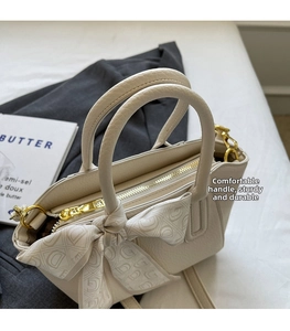 Detail of lychee textured leather bucket bag with silk scarf on cream white surface