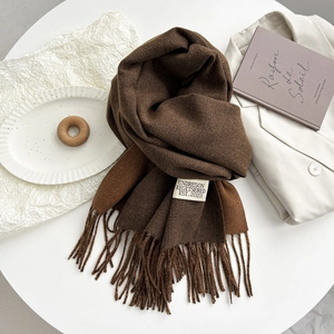 Detailed close-up of brown cashmere-style scarf tassels and brand label on beige blazer
