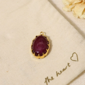 Close-up of a deep purple oval gemstone pendant on a beige fabric bag with dried flowers