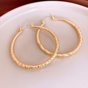 Close-up of gold metal hoop earrings with diamond-cut texture on white porcelain plate