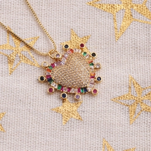Collier cœur rétro doré avec zircons colorés sur un tissu beige à motif étoilé