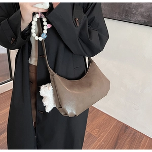 Brown faux leather crescent bag with white plush sheep charm on a model in a black trench coat