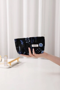 Detail of delicate blue flower embroidery on a black cotton linen makeup bag held by hand