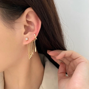 Detail view of a gold tassel ear cuff earring with crystal studs and hanging metal chains