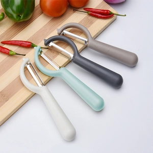 Multi-colored stainless steel fruit and vegetable peelers on a wooden board with fresh veggies
