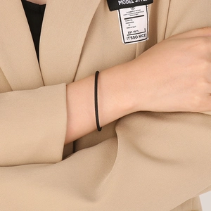 Close-up of a minimalist thin black cord bracelet on a model wrist with a beige suit