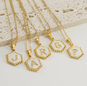 Detailed macro of gold hexagonal initial necklaces with white inlay on stone background