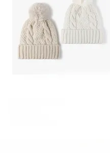 Dettaglio del berretto in maglia a trecce con pompon in ecopelliccia beige e bianco