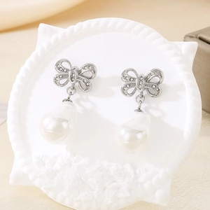 Detail of silver bow earrings with sparkling crystals and a white baroque pearl drop