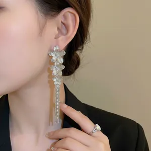 Elegant silver flower earrings with long shimmering diamond tassels worn by a model