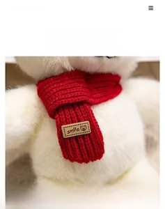Close-up of a white plush bear wearing a red knitted scarf with a Smile leather tag