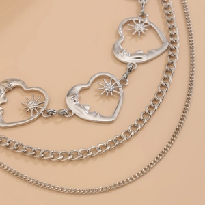 Macro detail of silver layered body chain with sunburst heart charm and curb chain links