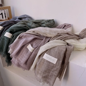 Close-up of stacked linen scarves in gray, green, and pink colors with fringe details