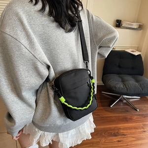 Detail of black nylon crossbody bag featuring a vibrant neon green braided chain strap