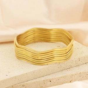 Detailed view of layered gold wavy bangles on stone surface with elegant satin background