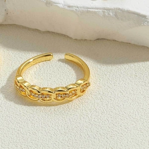 Close-up of gold chain link ring with sparkling zircons on minimalist stone background