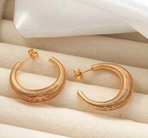 Detail of gold-plated twisted coil earrings resting on a beige velvet jewelry display