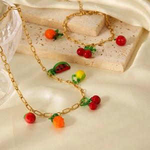 Detailed view of gold stainless steel necklace and bracelet with fruit charms on silk