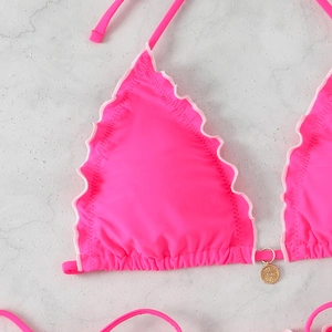 Detail of neon pink bikini top featuring frill trim and a golden sun charm accessory