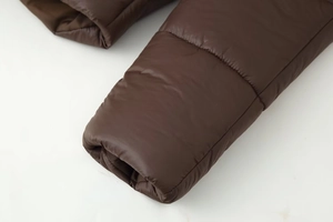 Gros plan détaillé de la manche de la doudoune marron montrant les coutures et le tissu