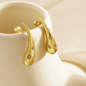 Elegant gold-plated teardrop earrings with crystals hanging on a ceramic vessel