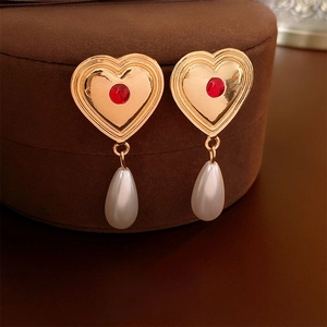 Close-up of heart pearl earrings with red stones on a velvet jewelry box
