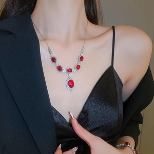 Close-up of a silver necklace featuring a red gemstone flower pendant worn by a model