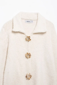 Détail du cardigan en fausse fourrure avec boutons fleurs en perles et tissu doux