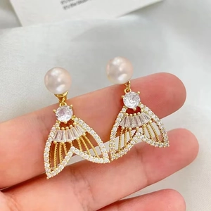 Gros plan de boucles d'oreilles perles dorées avec pendentif queue de sirène cristal