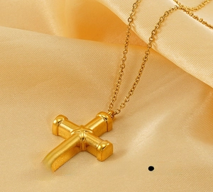 Macro shot of polished gold-plated stainless steel cross pendant on yellow satin
