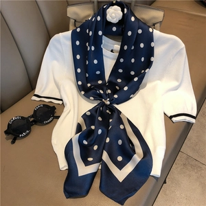 Detail of navy silk scarf with white polka dots and pearl buckle on white knit top