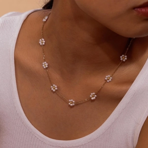 Close-up of golden flat cross chain with emerald flowers and white pearls on a model