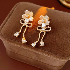 Détail de boucles d'oreilles fleur avec perle, nœud en strass et pendentifs zircon
