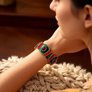 Close-up of vintage gold bangle with green enamel and purple gemstones on wrist