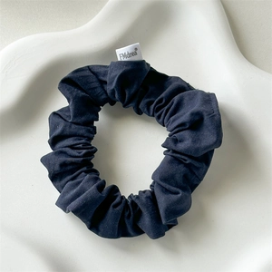 Detail of a dark blue cotton scrunchie with brand label on a white organic stand