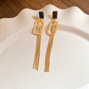 Détail de longues boucles d'oreilles à pompons dorés et éléments noirs sur plateau blanc